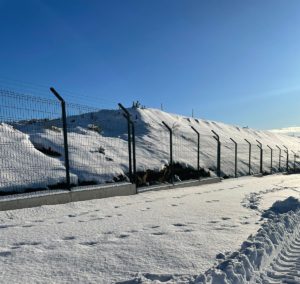 Malla perimetral galvanizada instalada sobre base de hormigón en terreno con nieve y clima extremo