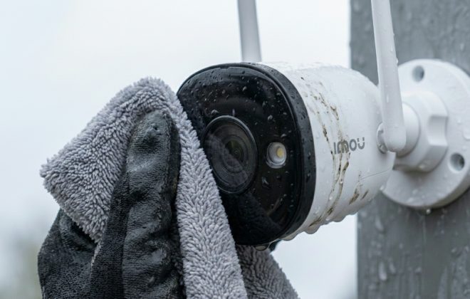 Limpieza del lente de una cámara de seguridad exterior con paño de microfibra durante un mantenimiento preventivo de vigilancia CCTV